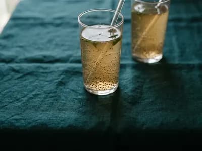 A tall glass of basil seed drink with suspended seeds visible against soft light