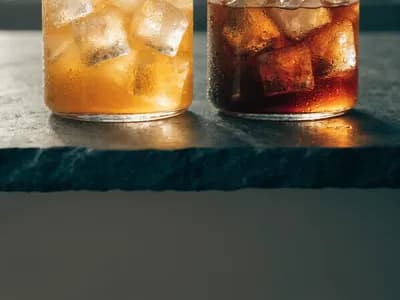 Tall glasses of iced citrus juice and cold coffee with condensation, on a dark stone counter
