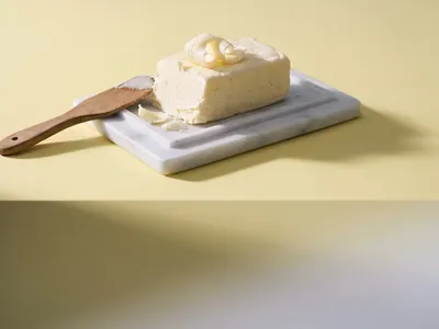 A block of churned butter with curled shavings on a marble dish against primrose yellow