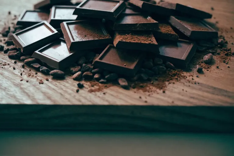 Broken squares of dark chocolate, cocoa nibs and dusted cocoa powder on a dark walnut wood board