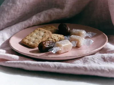 Biscuits, soft dates and wrapped sweets on a dusty rose-pink plate and matching linen cloth