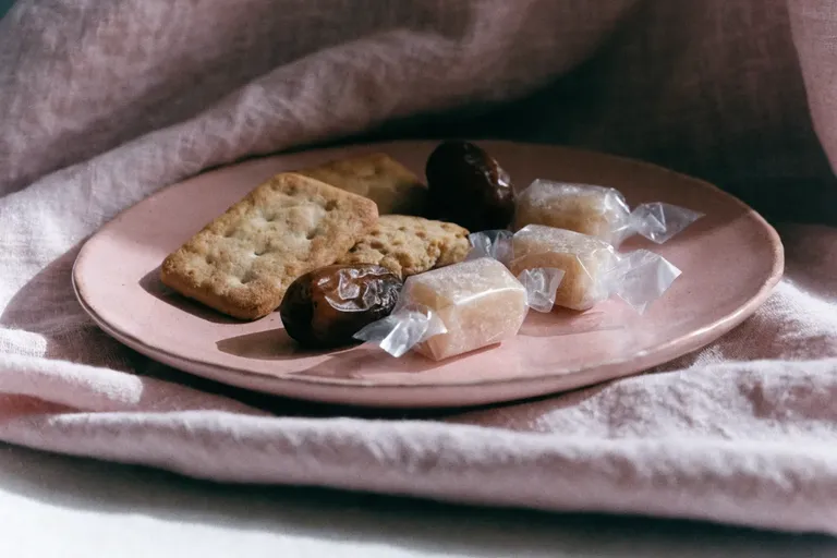 Biscuits, soft dates and wrapped sweets on a dusty rose-pink plate and matching linen cloth