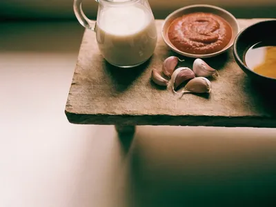 Coconut milk, tomato paste, garlic and cooking oil arranged on a weathered wooden board