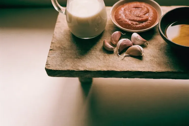 Coconut milk, tomato paste, garlic and cooking oil arranged on a weathered wooden board