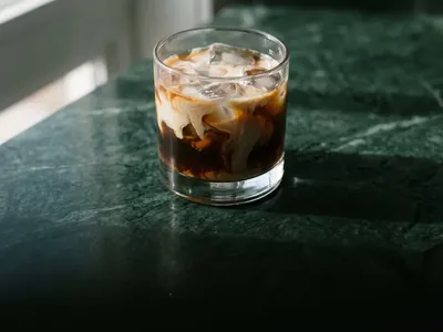 Cold brew iced coffee with swirling cream and ice cubes on forest green marble