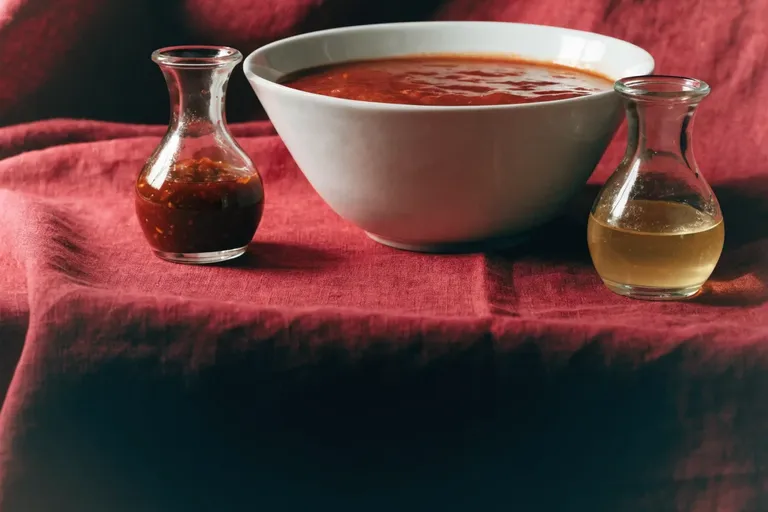 A wide bowl of red tomato sauce with chilli sauce and vinaigrette in glass cruets on a deep red linen cloth