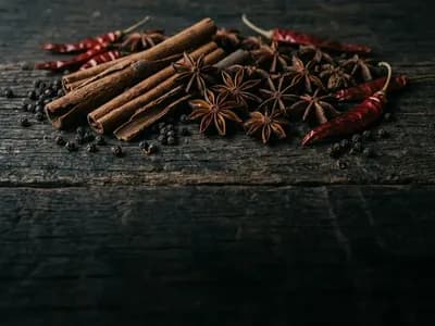 Cinnamon quills, star anise, black peppercorns and dried red chillies heaped on dark weathered wood