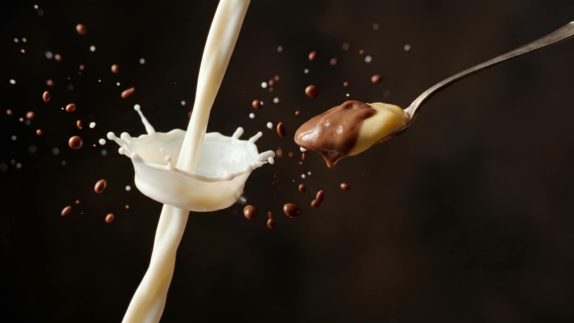 A pouring stream of fresh milk twisting into a soft crown splash beside a spoonful of thick chocolate pudding