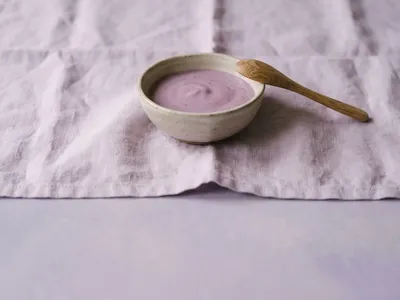 Smooth fruit puree in a handcrafted ceramic bowl with a wooden spoon on a lilac cloth