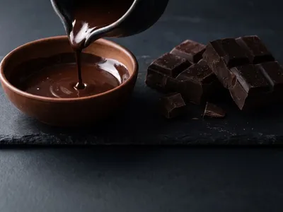 Glossy melted dark cooking chocolate drizzling into a bowl beside chocolate blocks