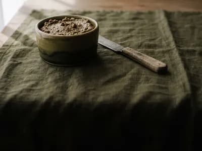 A ceramic ramekin of savoury sandwich spread with a spreading knife on a moss green cloth
