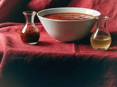 A wide bowl of red tomato sauce with chilli sauce and vinaigrette in glass cruets on a deep red linen cloth