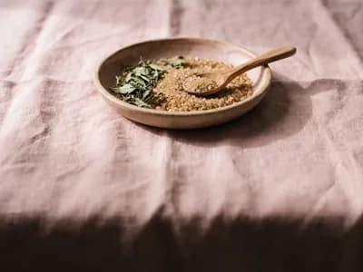 Raw sugar crystals and stevia leaves in an earthenware dish on a blush rose cloth